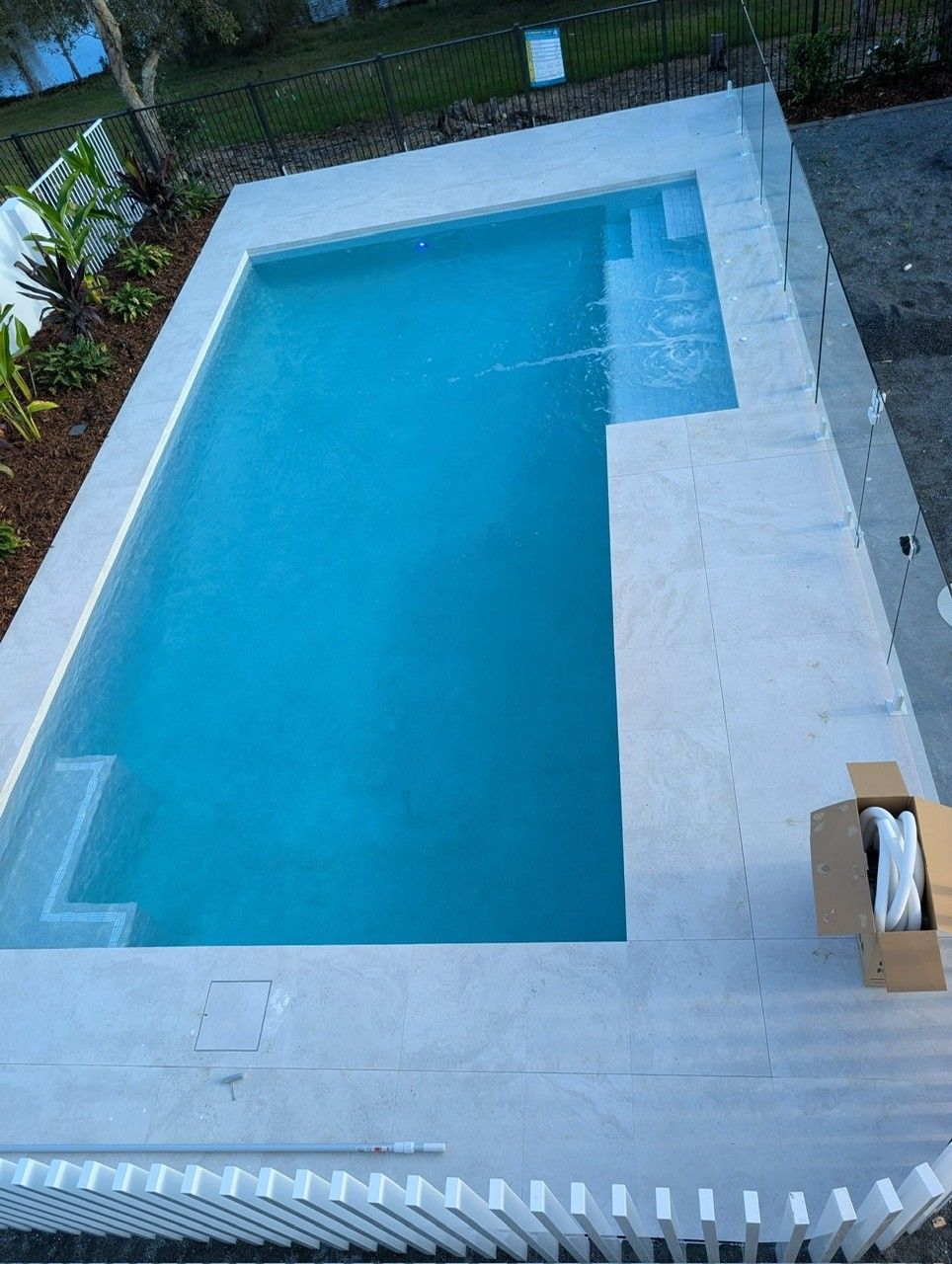 Rectangular blue swimming pool with a white deck and steps, viewed from above