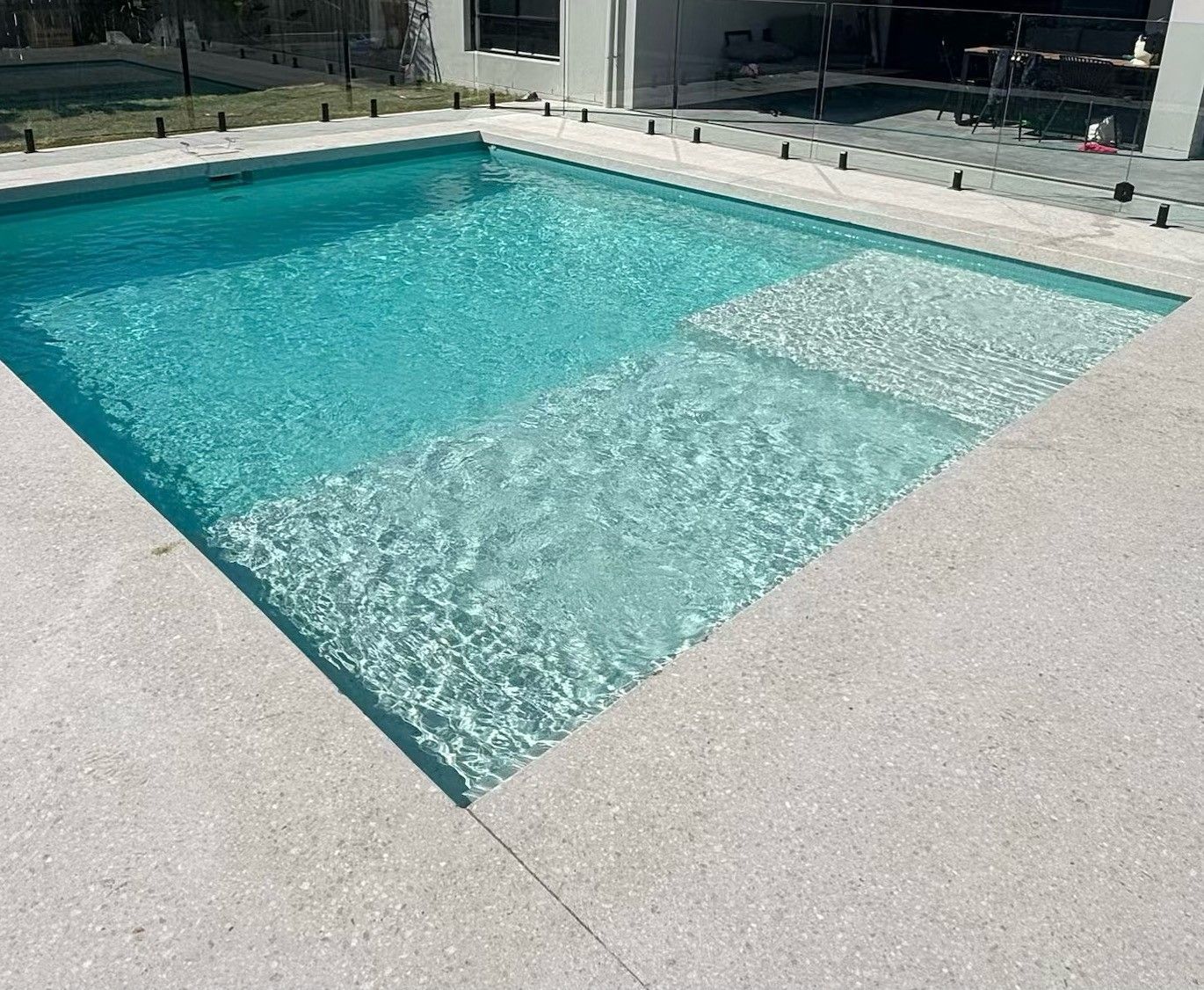 Rectangular swimming pool with turquoise water and a shallow tanning ledge beside a light concrete deck