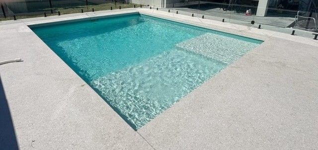 Rectangular turquoise swimming pool with a shallow ledge and white deck tiles
