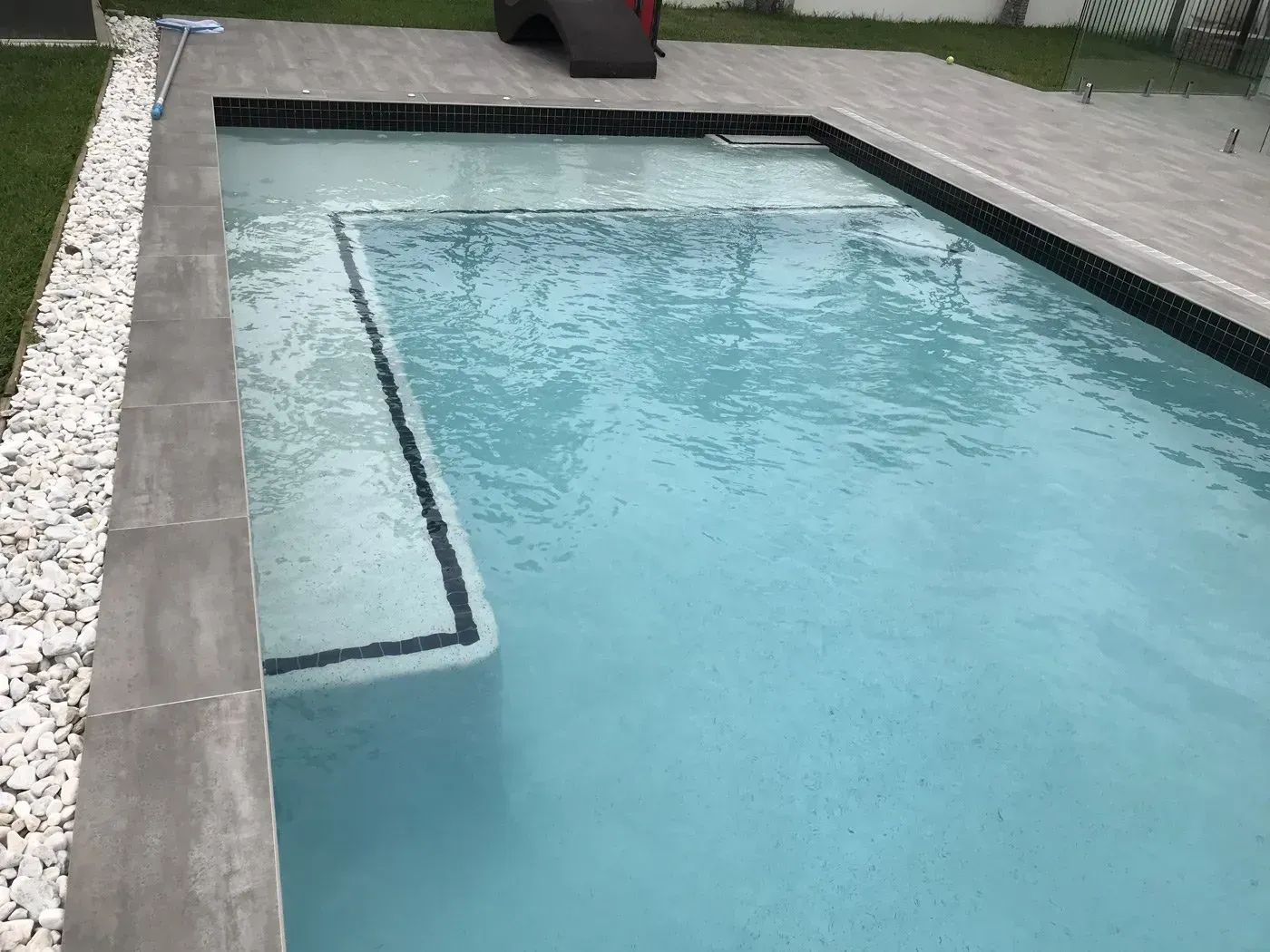 Rectangular backyard swimming pool with light blue water and stone decking
