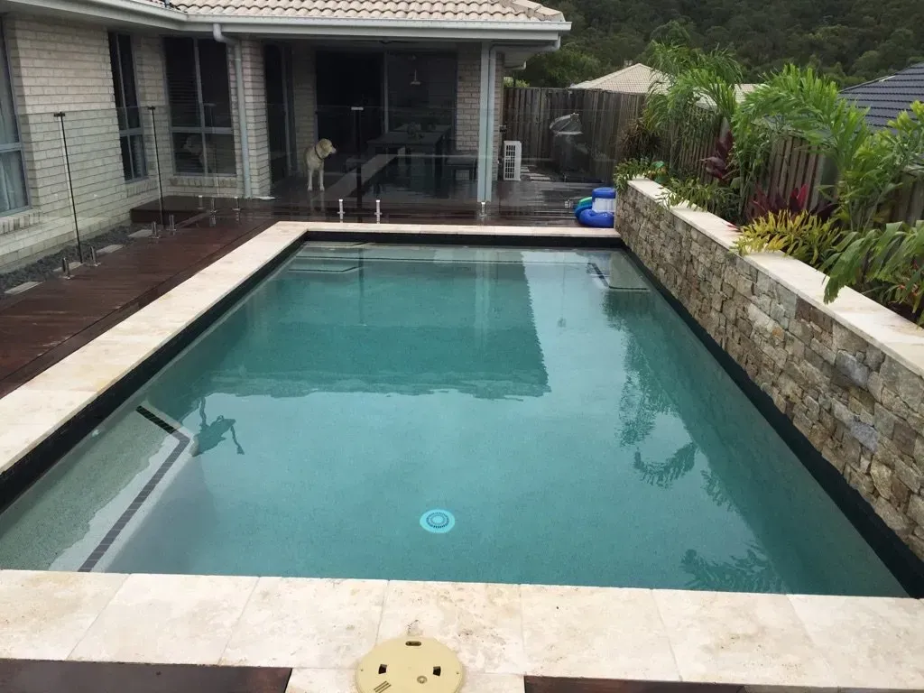 Rectangular backyard swimming pool beside a stone wall and patio under a covered porch