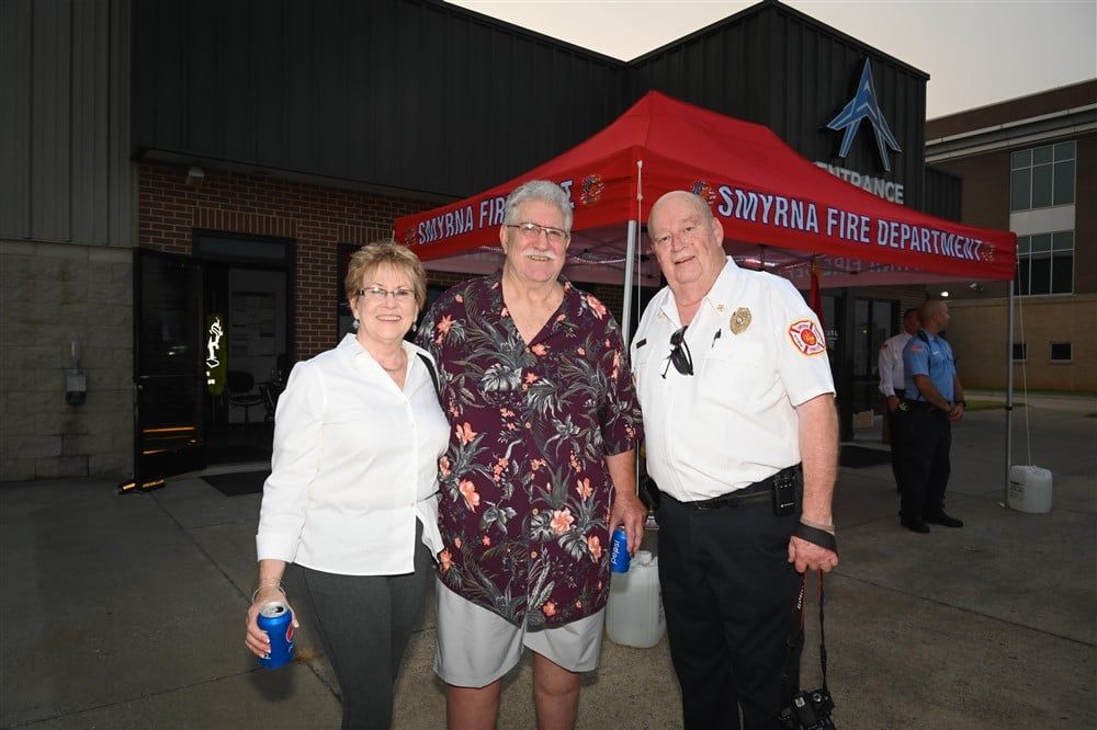 Three people are posing for a picture in front of a fire department building.