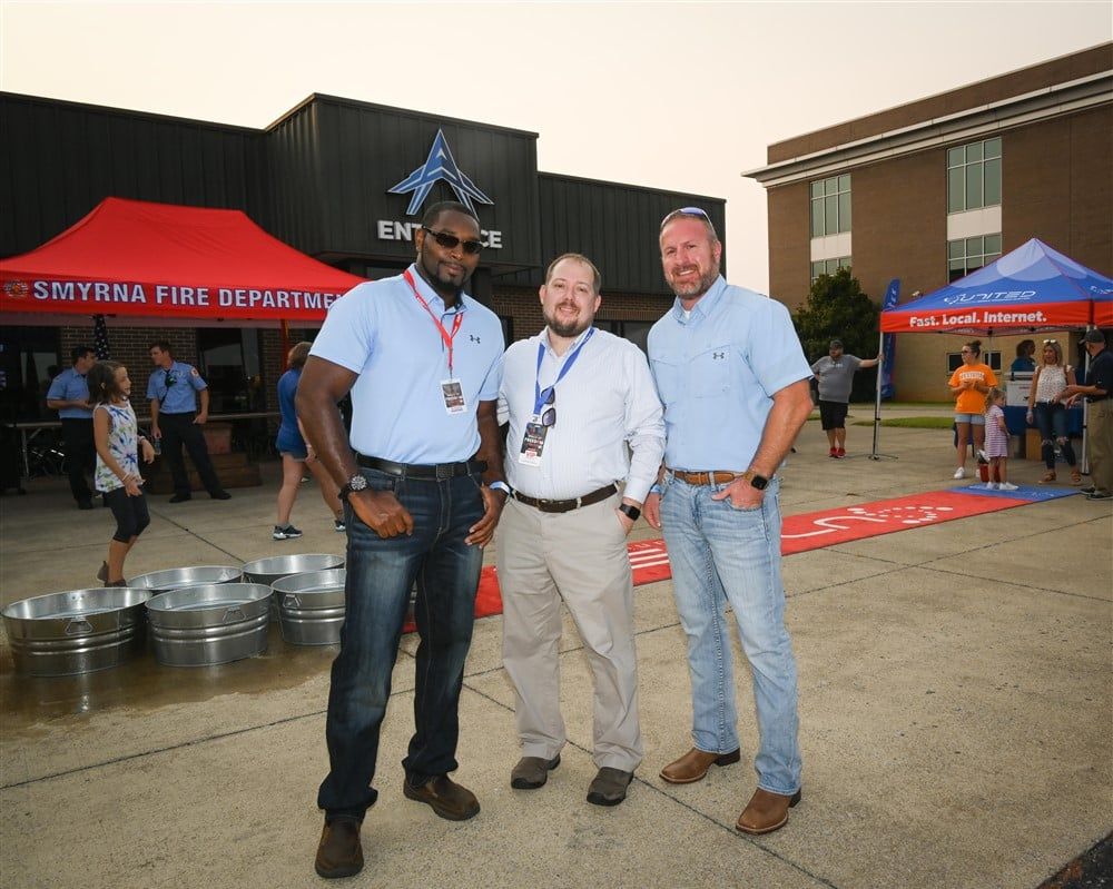 Three men are posing for a picture in front of a fire department building