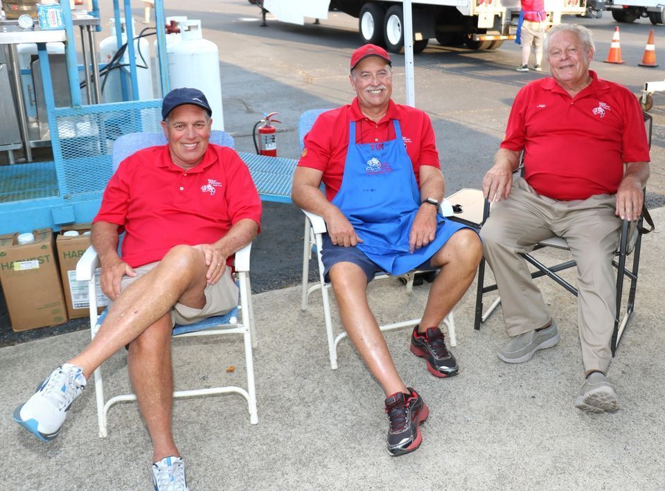 Three men in red shirts and blue aprons are sitting in chairs