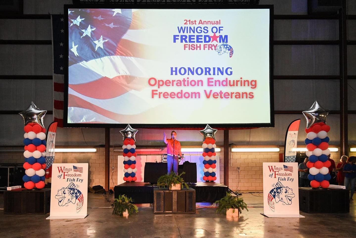 A man is standing in front of a large screen that says honoring operation enduring freedom veterans.