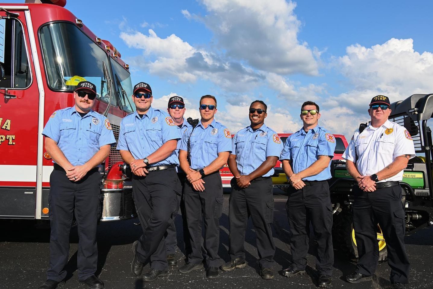 A group of firefighters are posing for a picture in front of a fire truck.