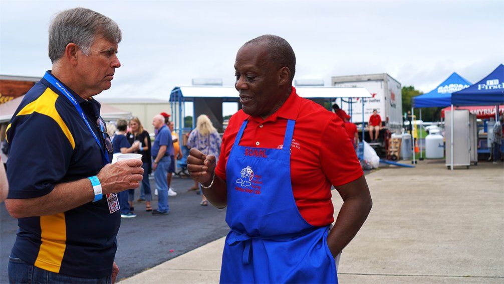 Two men in aprons are talking to each other in a parking lot.