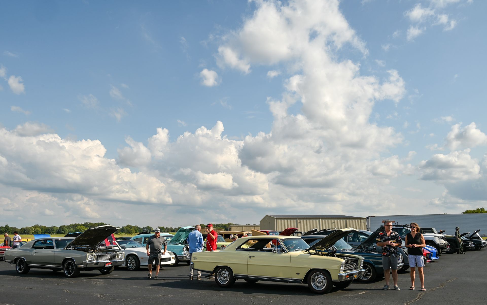 A group of people are standing in front of a parking lot full of cars.