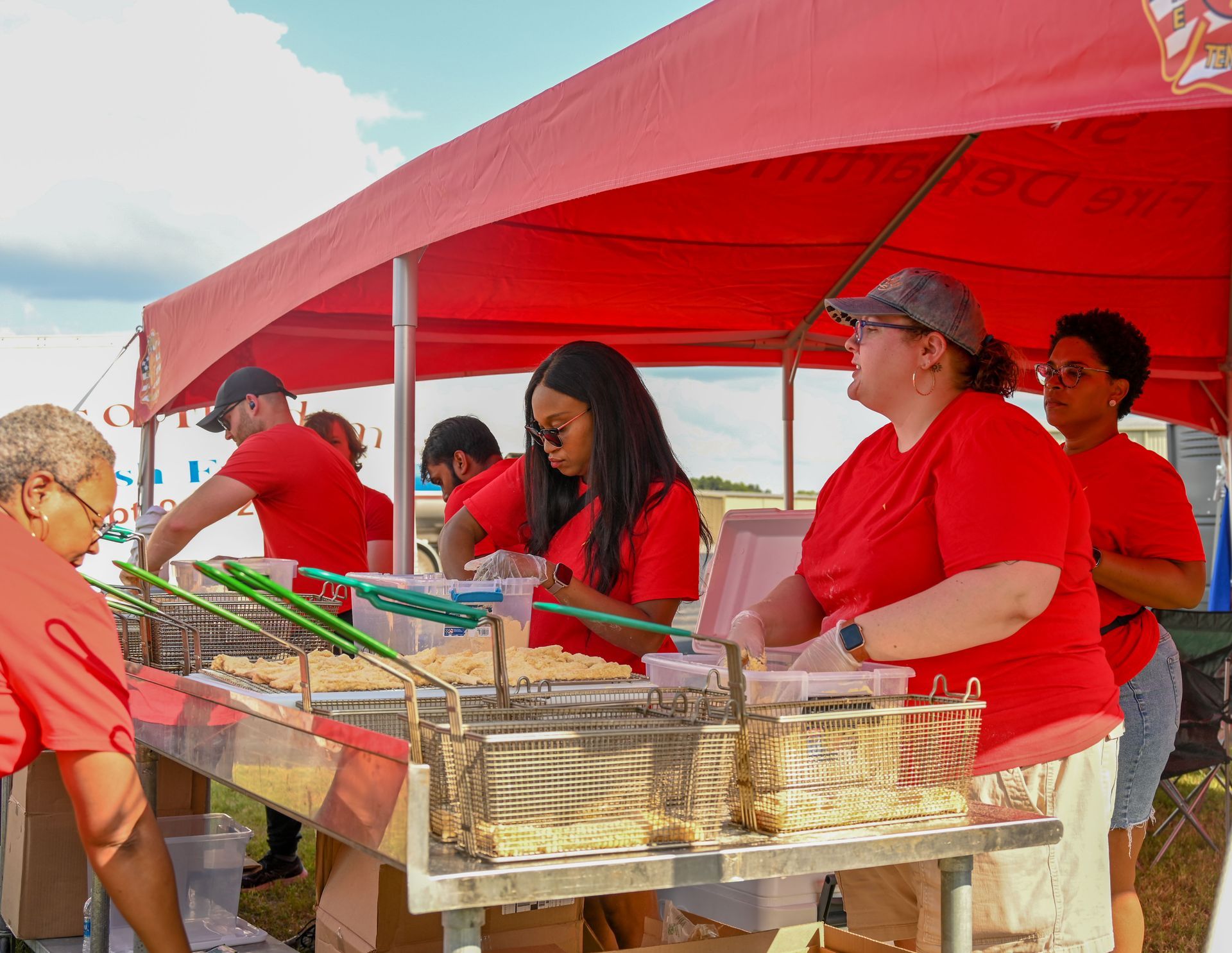 A group of people in red shirts are working at a food stand under a red tent.