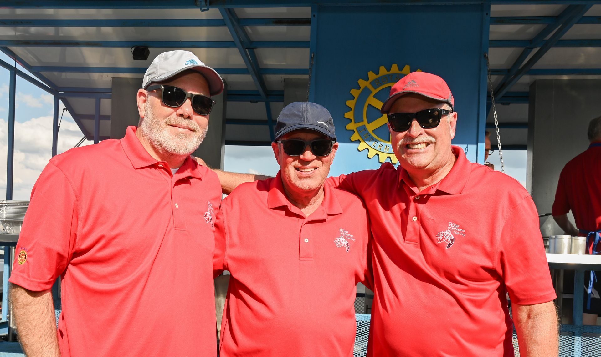 Three men wearing red polo shirts and hats are posing for a picture.