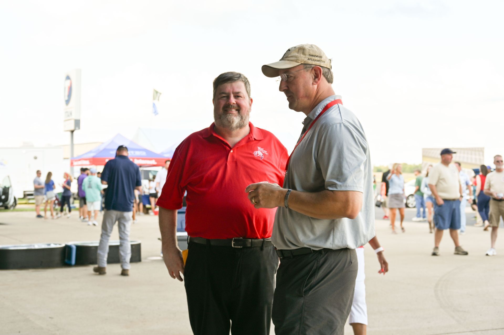 Two men are standing next to each other and talking in a crowded area.