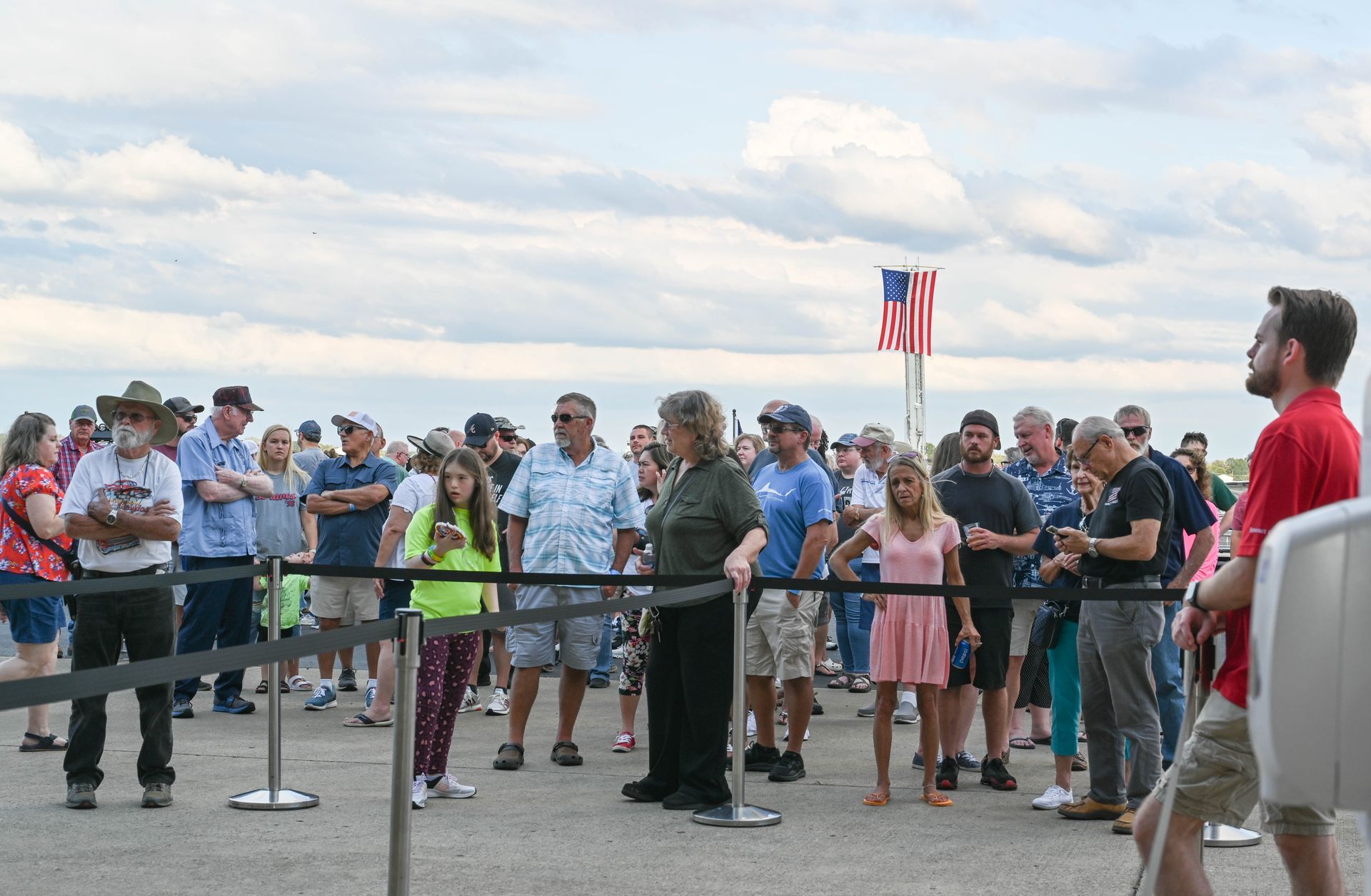 A man in a red shirt is standing in front of a crowd of people.
