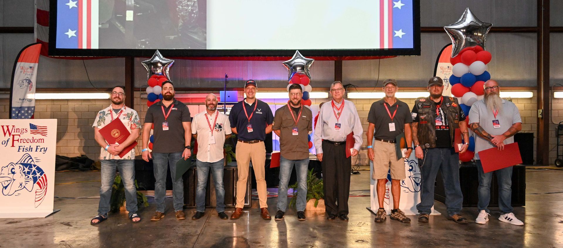 A group of men are standing in front of a large screen.