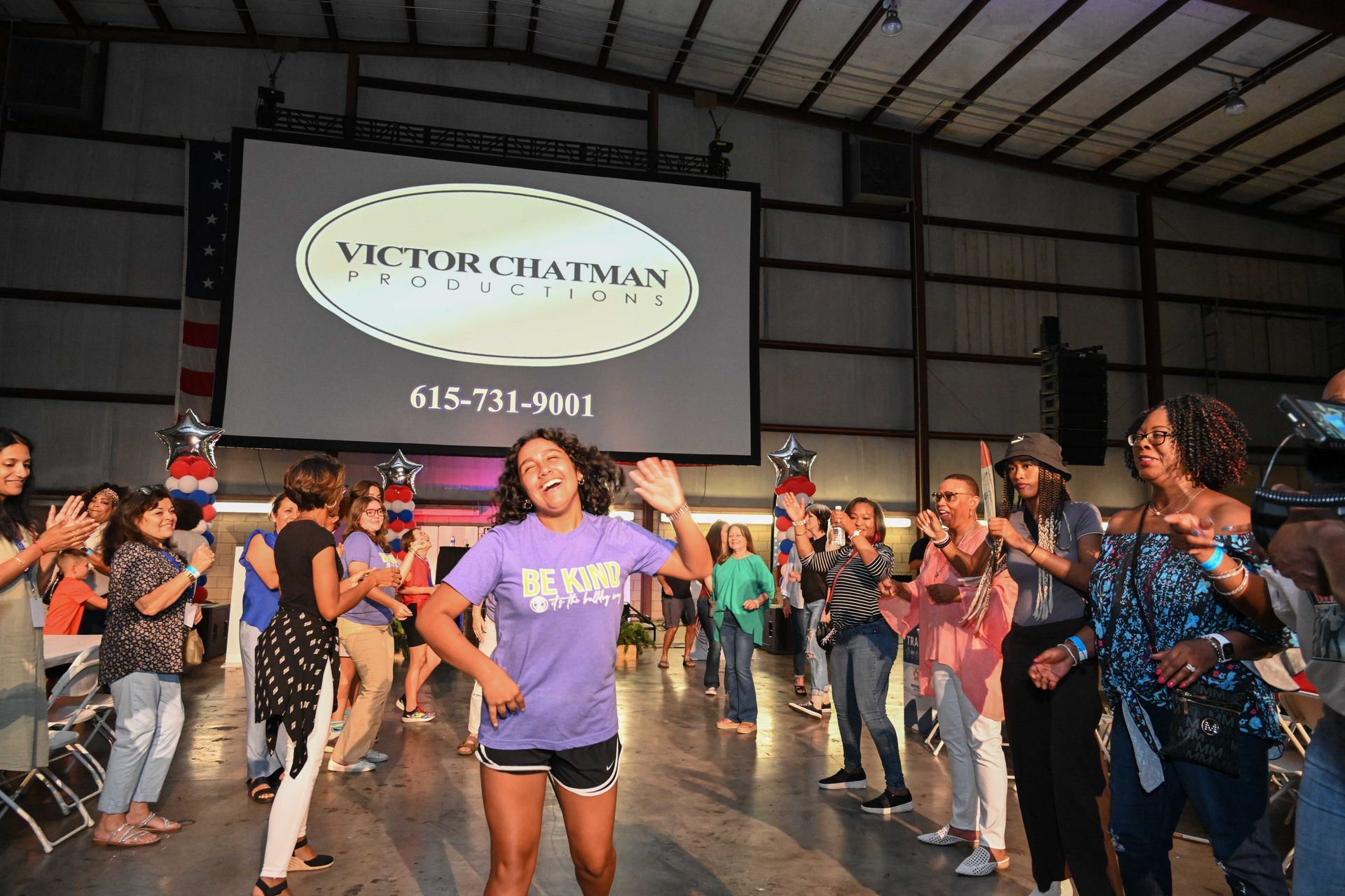 A group of people are dancing in front of a large screen that says victor chatman