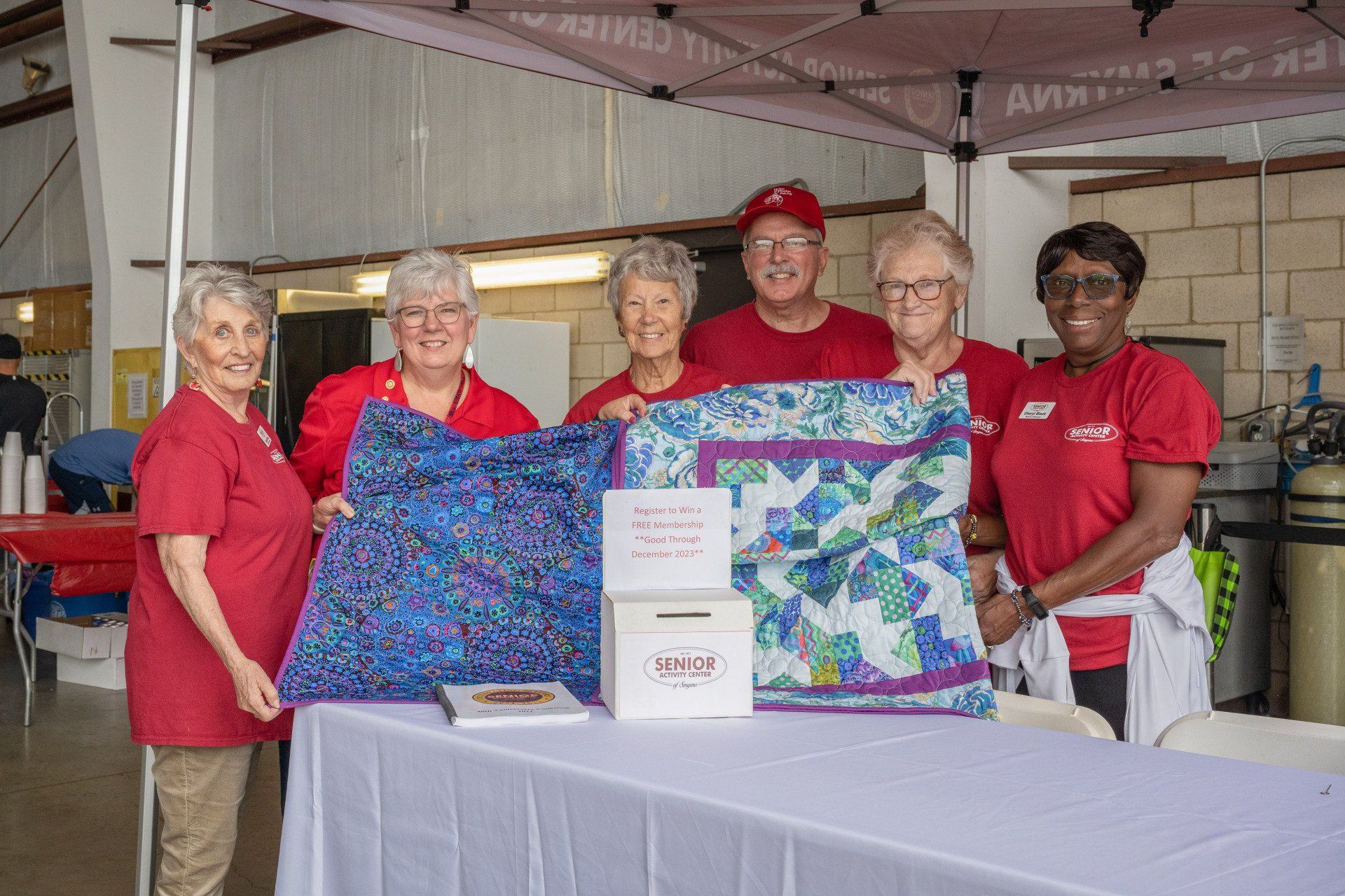A group of people are standing around a table holding a quilt.