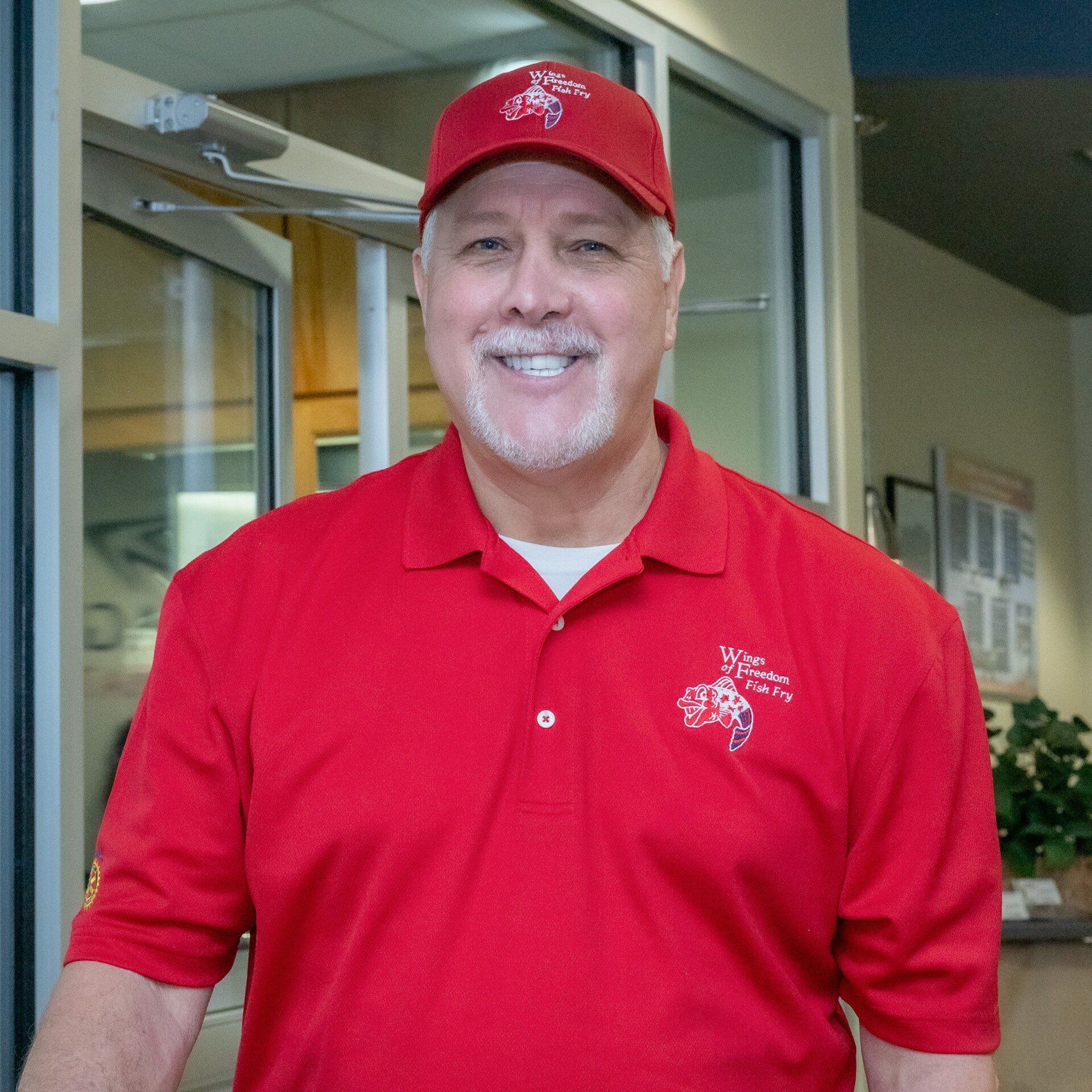 A man in a red shirt and hat is smiling for the camera