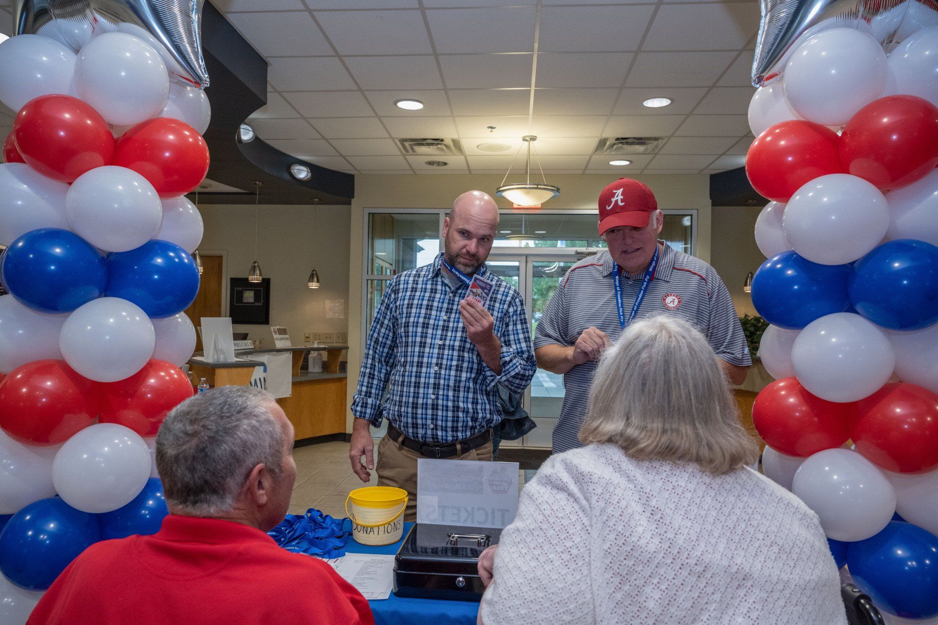 A group of people standing around a table with red , white and blue balloons.