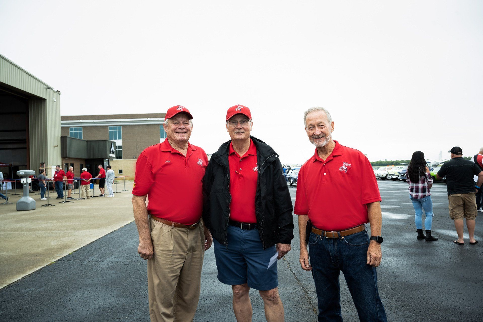 Three men in red shirts are standing next to each other in a parking lot.