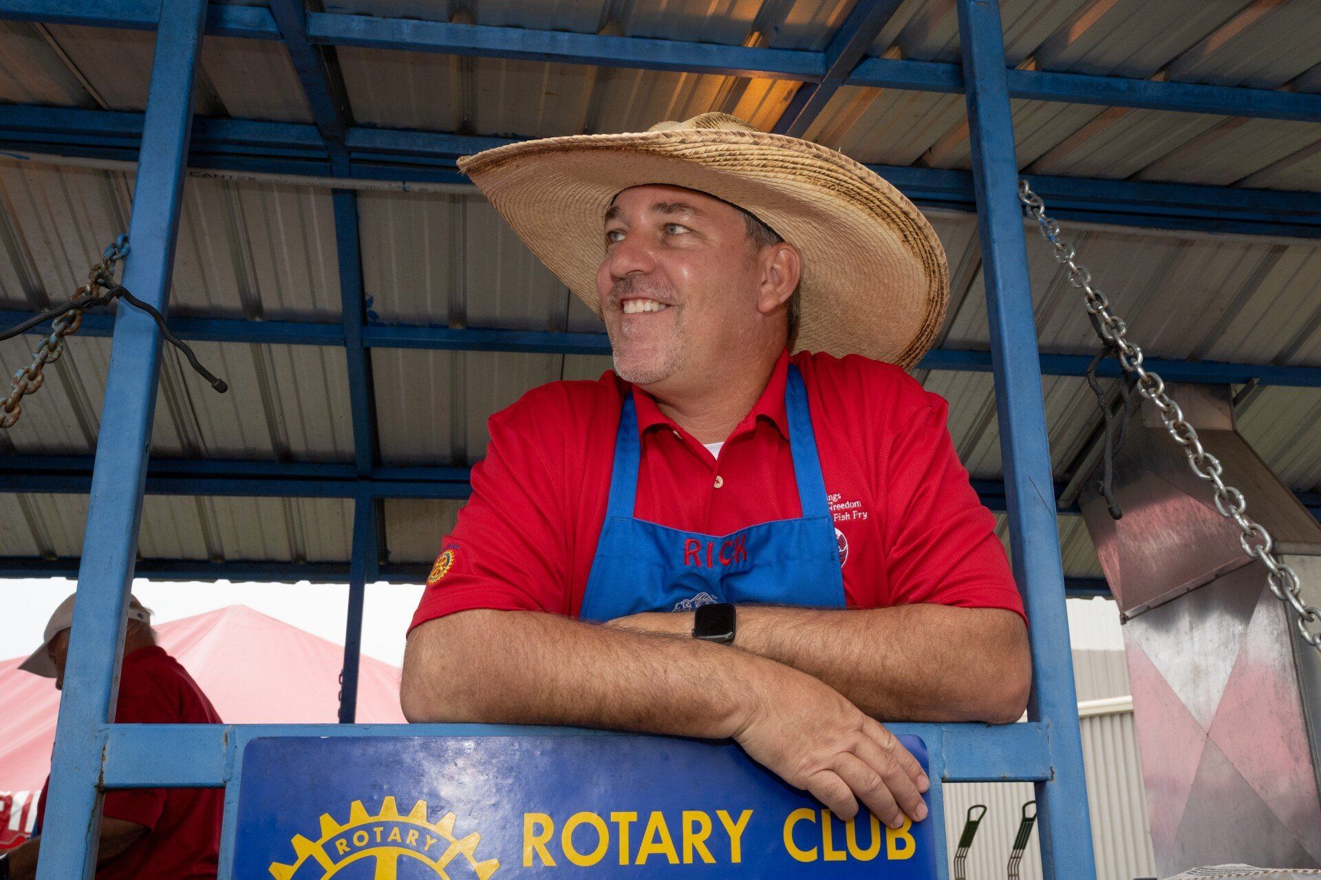 A man wearing a straw hat is leaning on a sign that says rotary club