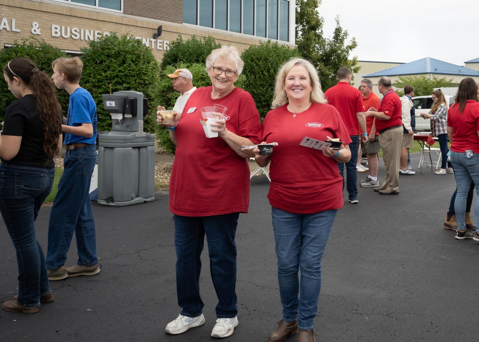 Two women in red shirts are standing in front of a building with the word business on it.