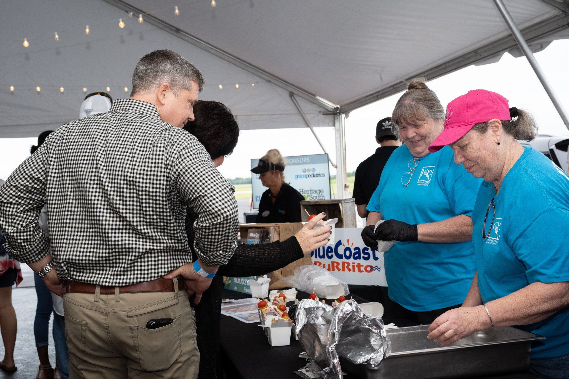 A group of people are standing around a table under a tent.