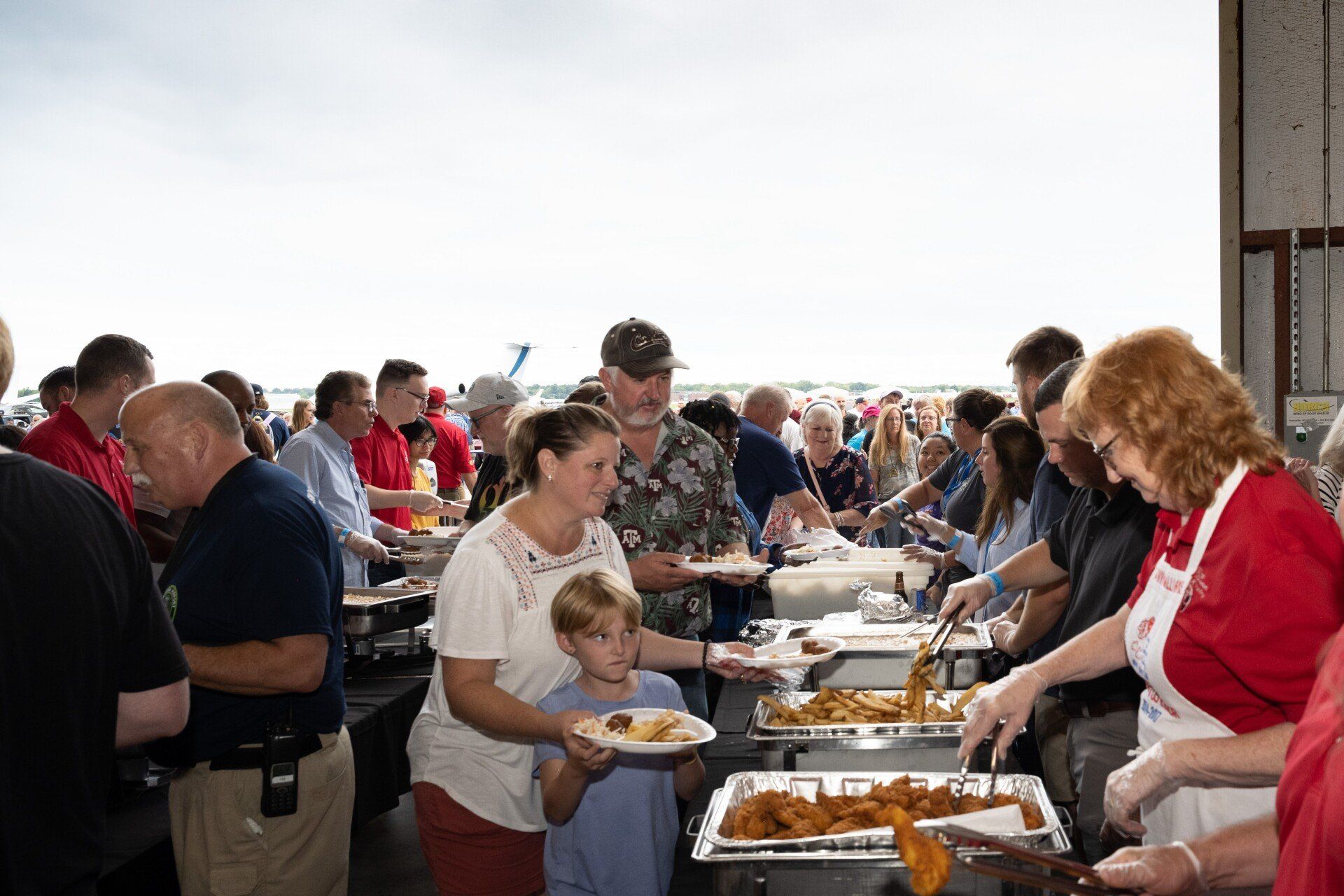 A large group of people are standing around a table eating food.