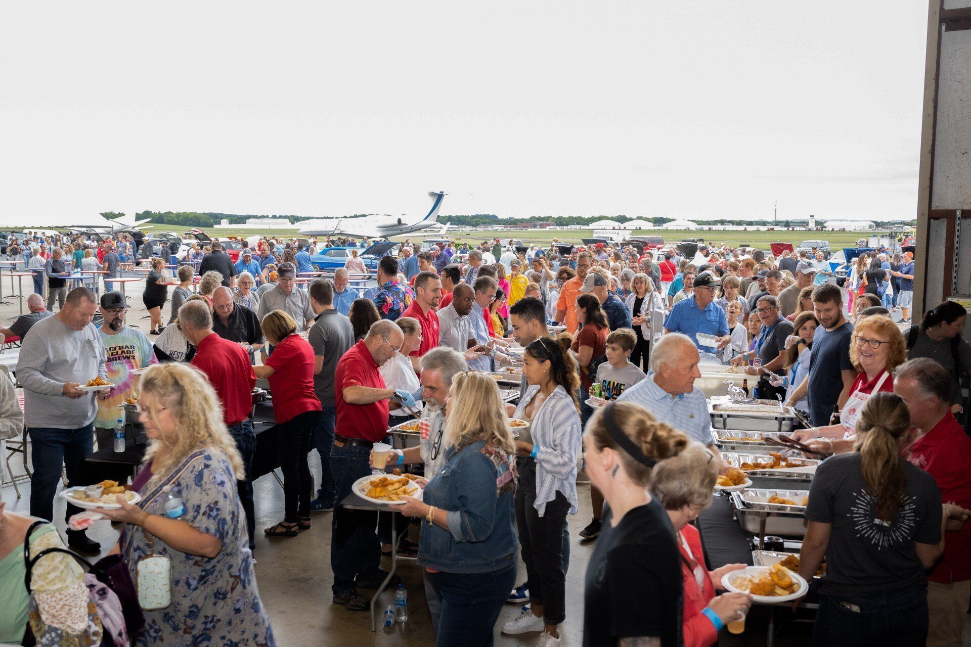 A large group of people are standing around tables eating food.