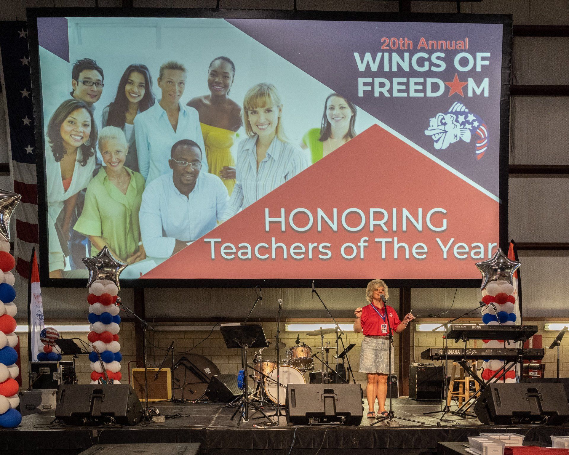 A woman is standing on a stage in front of a large screen that says honoring teachers of the year