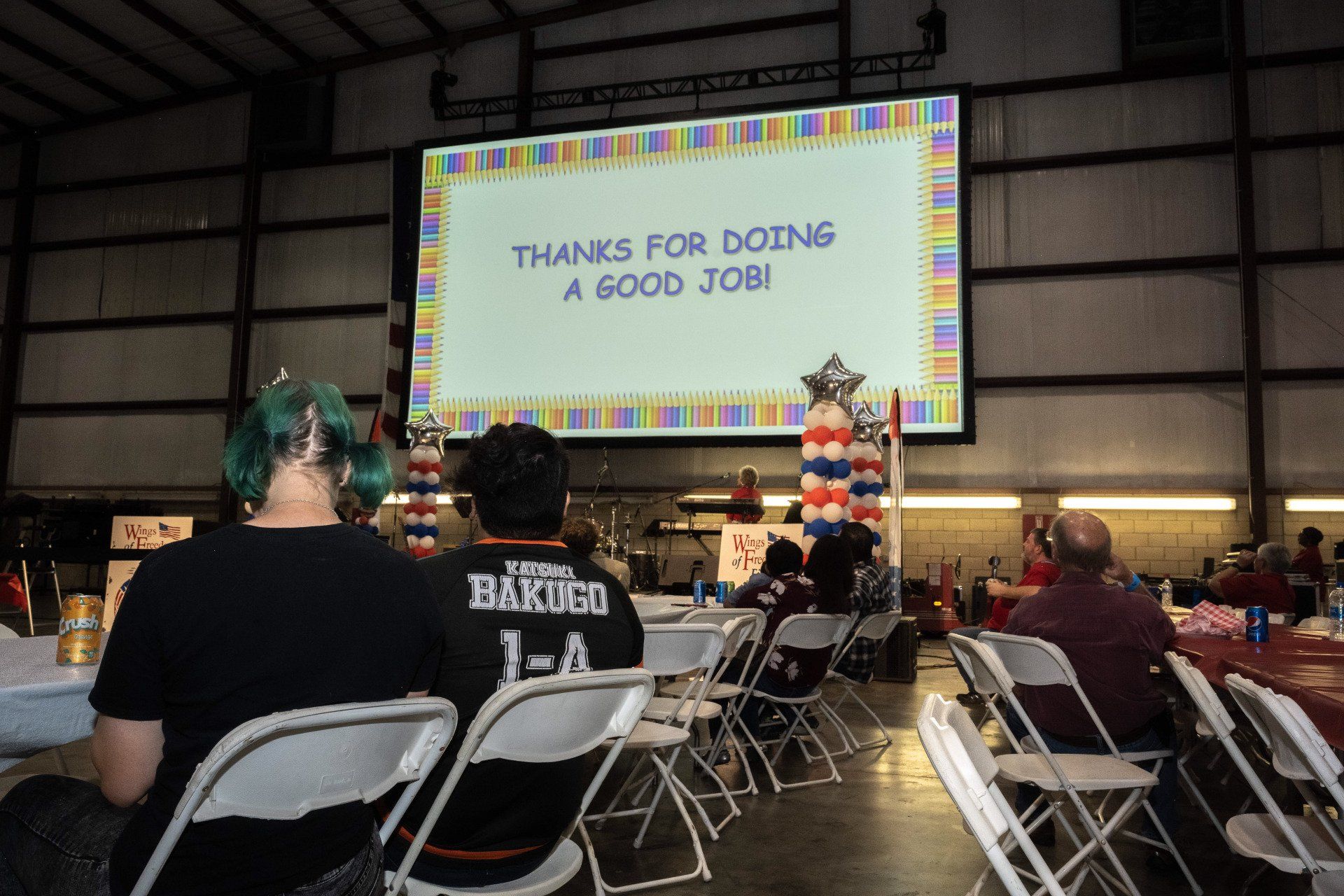 A group of people are sitting in chairs in front of a large screen that says thanks for doing a good job