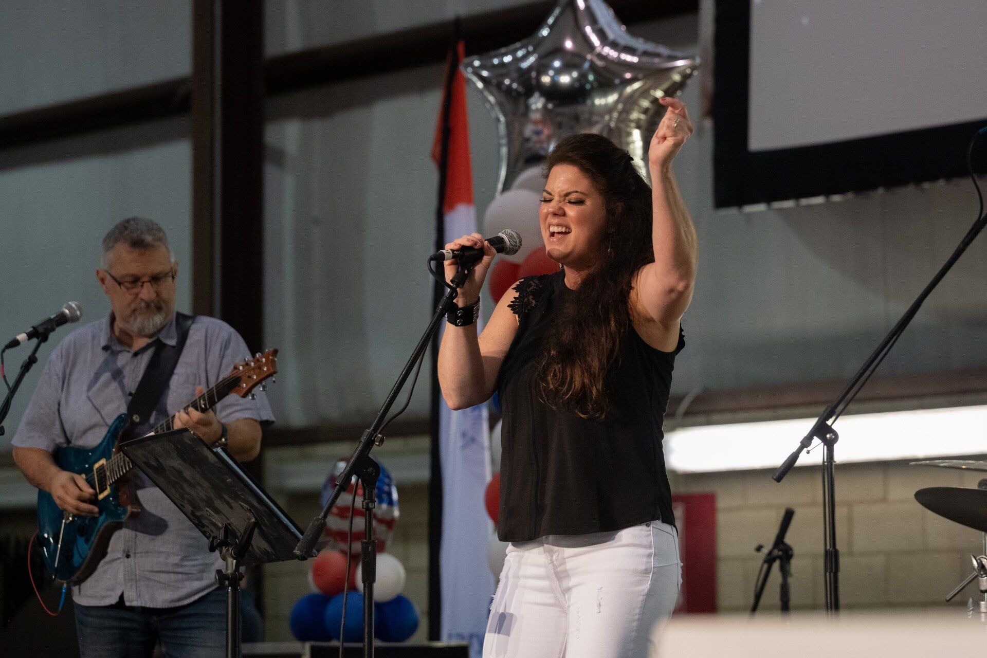 A woman is singing into a microphone while a man plays a guitar.