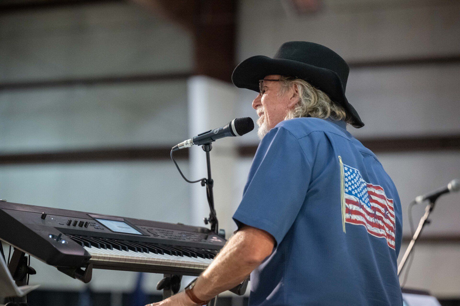 A man in a cowboy hat is playing a keyboard and singing into a microphone.