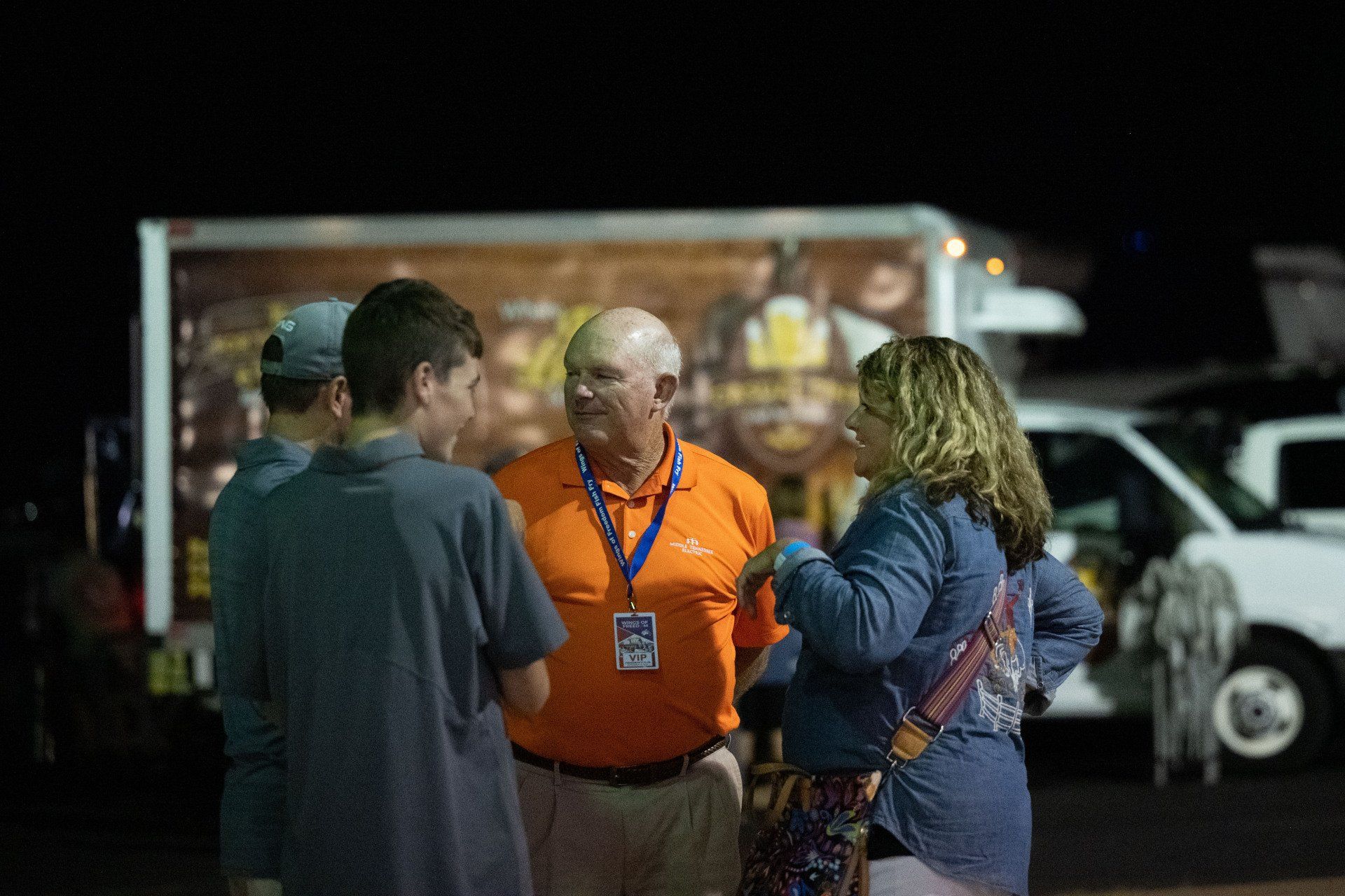 A group of people are standing next to each other in front of a truck at night.