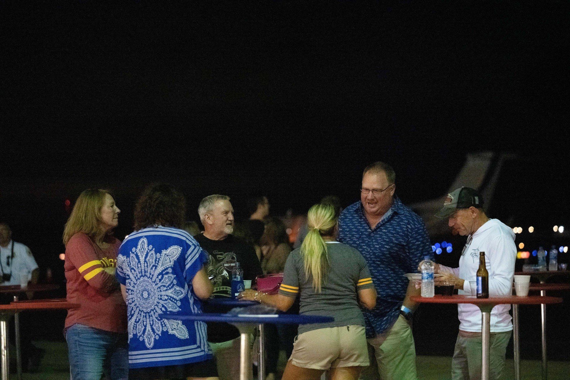 A group of people are standing around tables at night