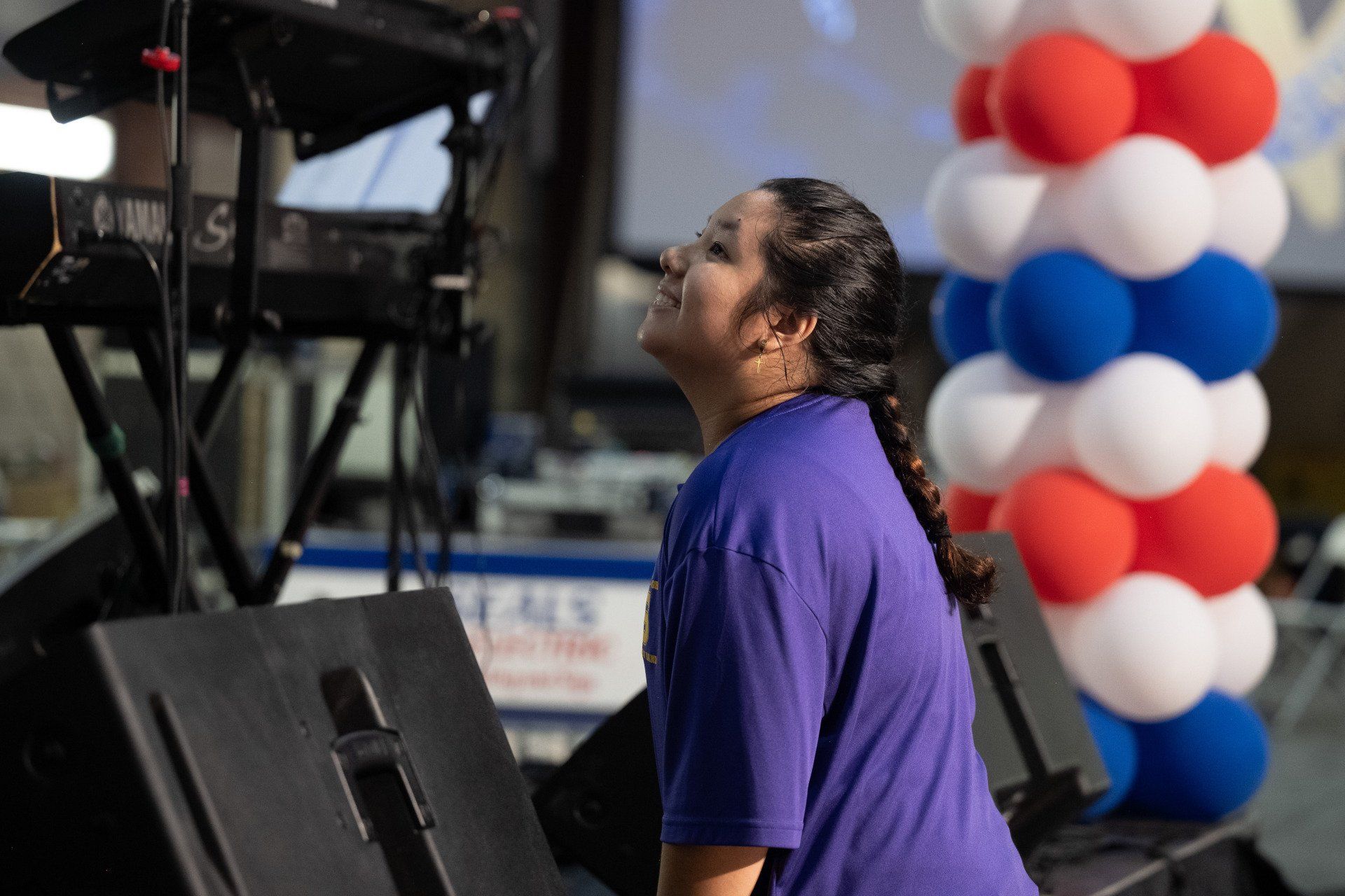 A woman in a purple shirt is standing in front of a keyboard and balloons.
