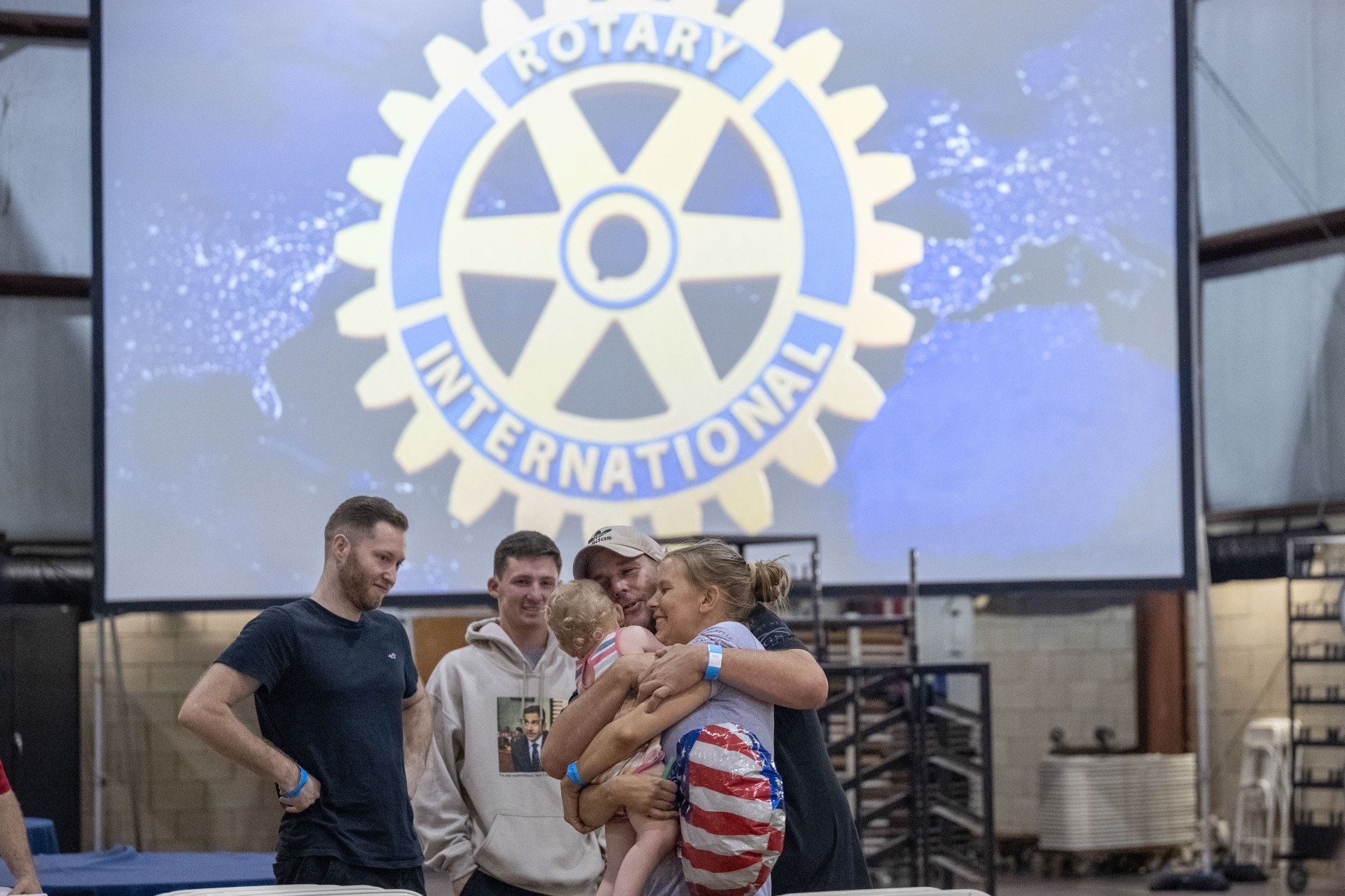 A group of people are standing in front of a large screen with a rotary international logo on it.