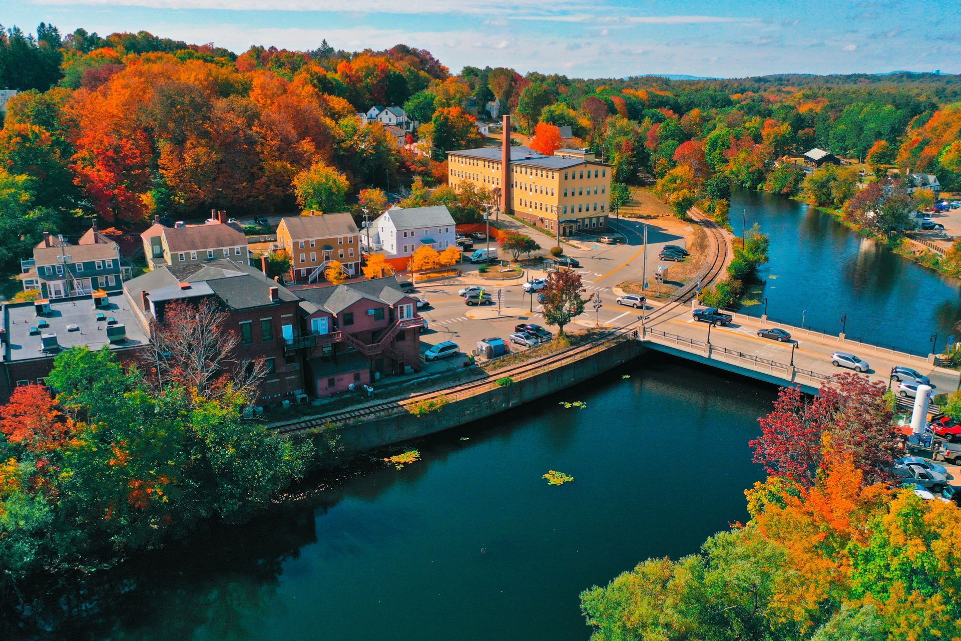 Autumn riverside town with a bridge, buildings, and colorful trees beside calm water