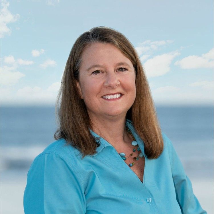 Woman in a turquoise blouse smiling by the ocean with blue sky in the background