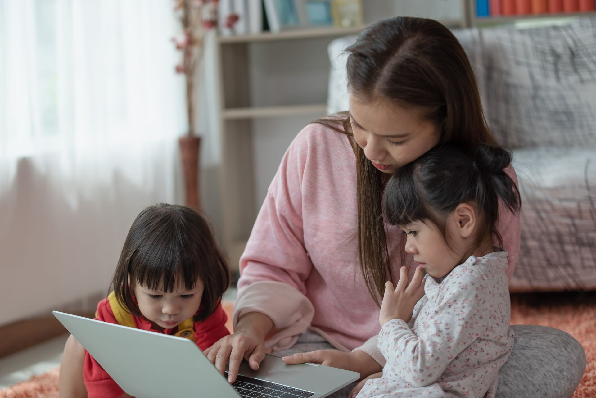 Three children gathered around a laptop, one adult helping in a cozy living room