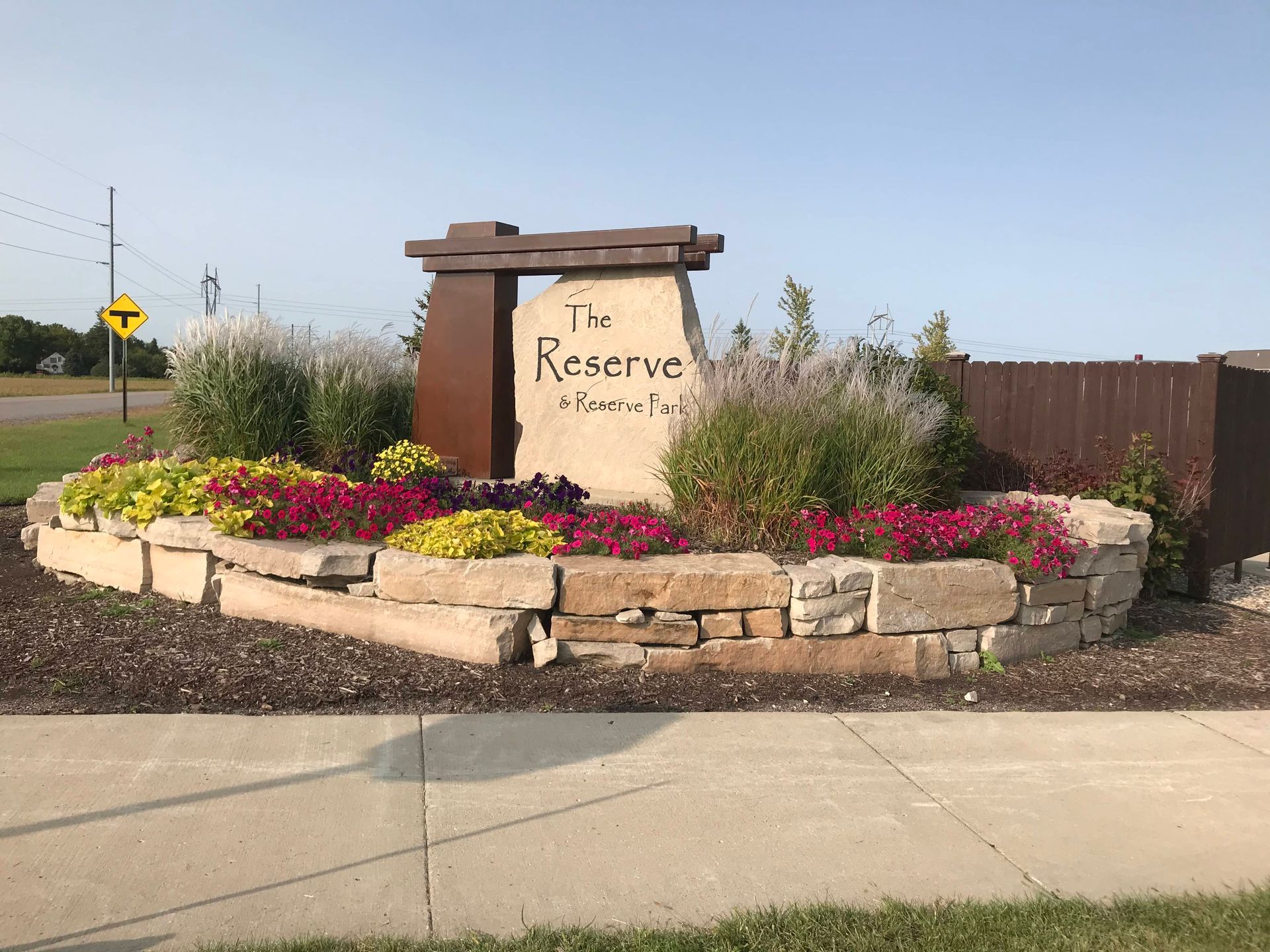 A sign for The reserve is surrounded by flowers and rocks.