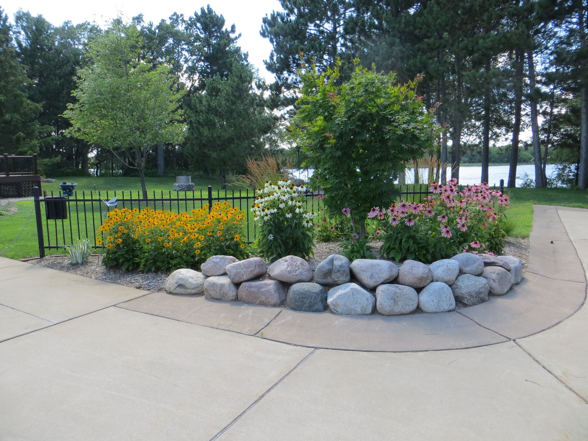 A garden with flowers and rocks in the middle of a backyard sidewalk