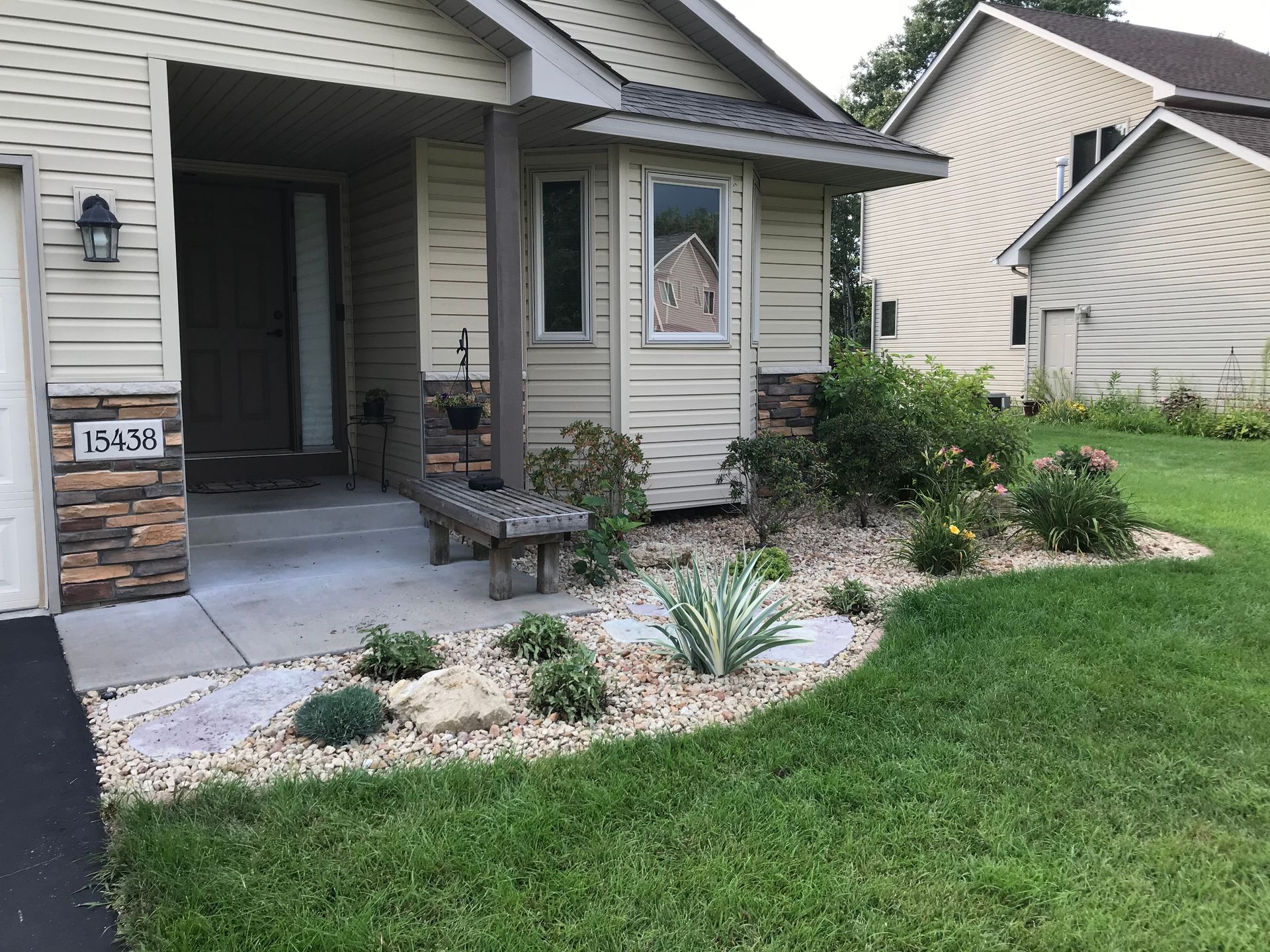 A rock garden with various plants in front of a house. 