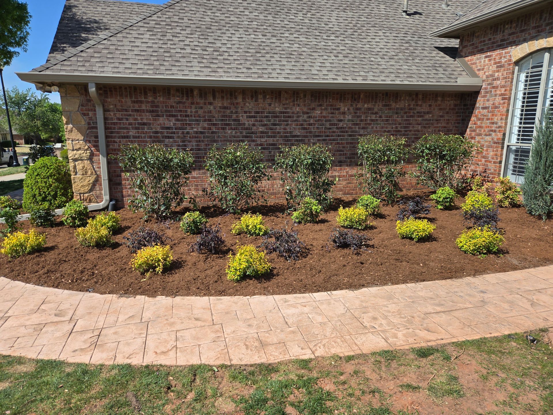 Brick house front yard with a curved mulch bed, small shrubs, and a stone walkway