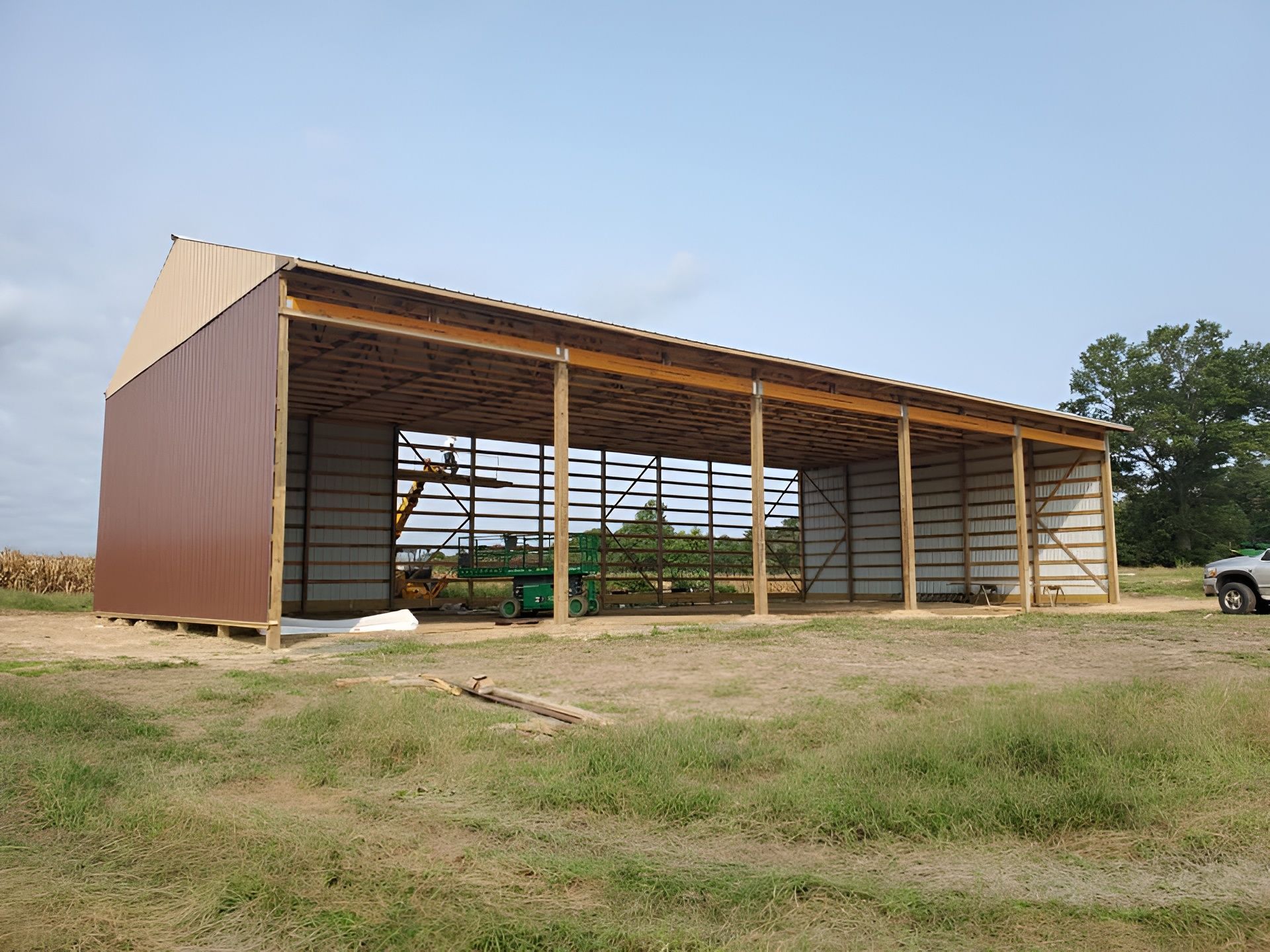 A partially constructed pole barn with brown metal siding on one end and open wooden framing on the side.