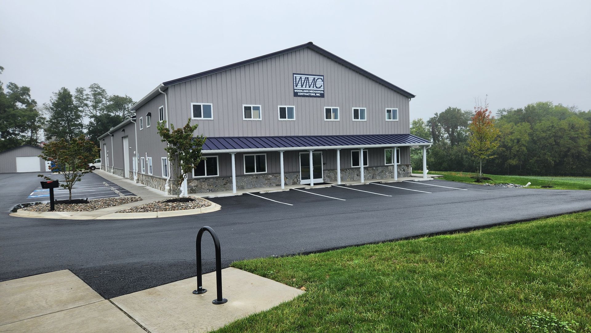 A two-story gray metal warehouse building with a stone-accented facade, covered porch, and a freshly paved asphalt lot.