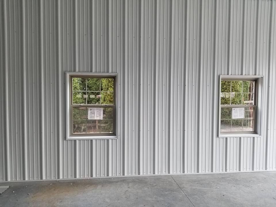 Two rectangular windows are set into a wall covered with vertical white corrugated metal siding.