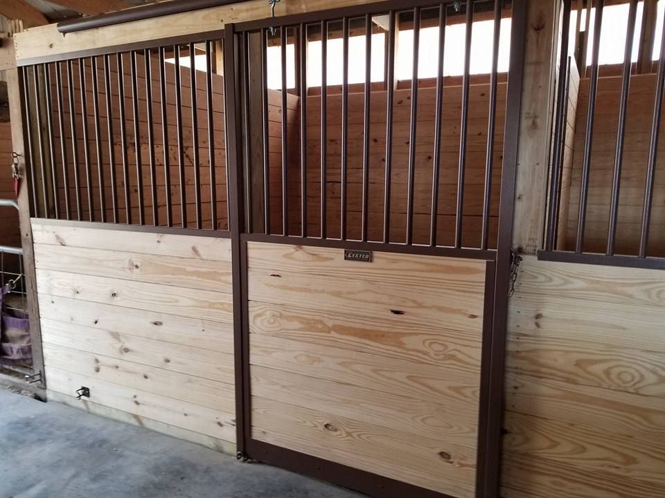 Stable stalls with light-colored wooden walls and dark metal grilles under a wooden roof.