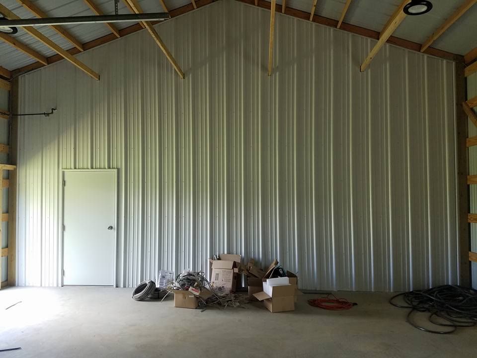 Interior of a metal building with a white ribbed wall, a single door, and boxes scattered on the concrete floor.