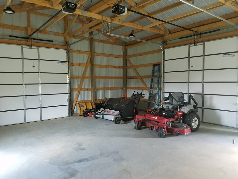 A wide-angle interior view of a bright garage with two closed white doors, a red riding mower, and equipment stored inside.