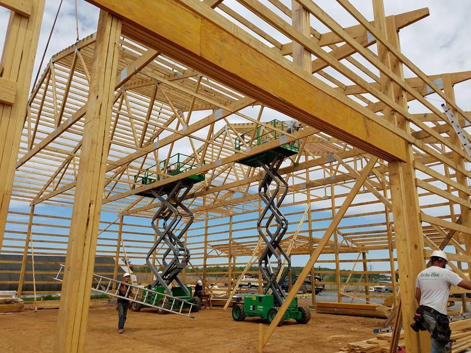Two construction workers operate scissor lifts inside a large timber-framed building under construction.