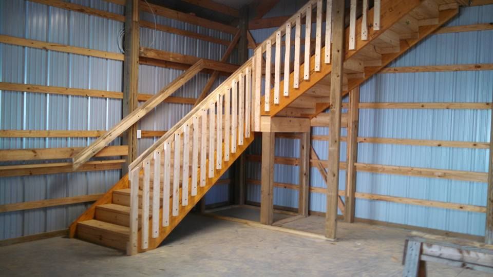 A wooden staircase with balusters rises along a metal-sided wall inside a garage or barn-style building.
